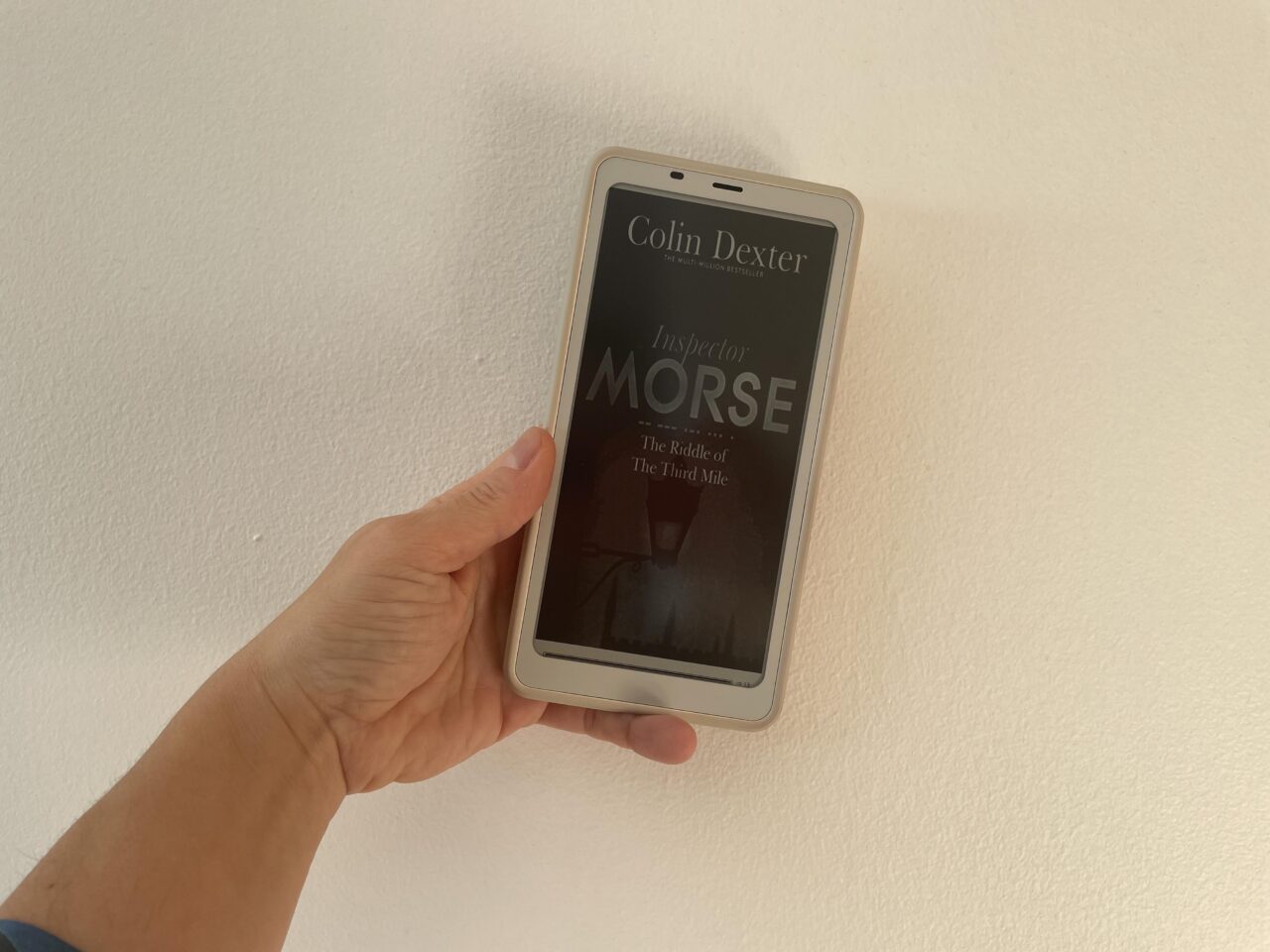 Ebook cover of The Riddle of the Third Mile by Colin Dexter held by my left hand, in a diagonal angle and against a white background.