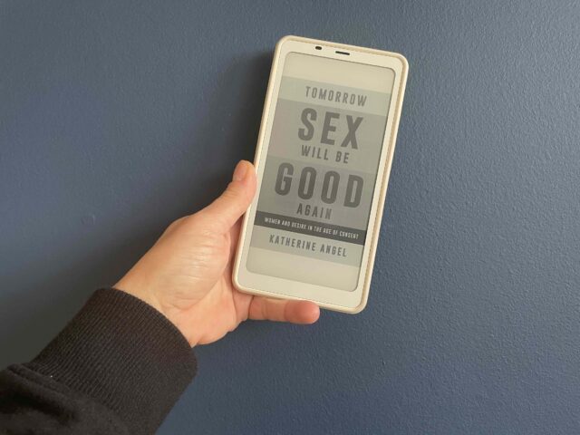 Cover of ebook of Tomorrow Sex will be good again by Katherine Angel with my hand holding it at an angle against a blue background