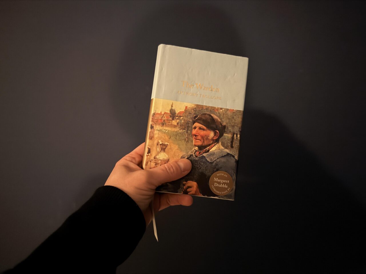 Copy of Macmillan Collector's edition of The Warden held by my hand against a navy background.