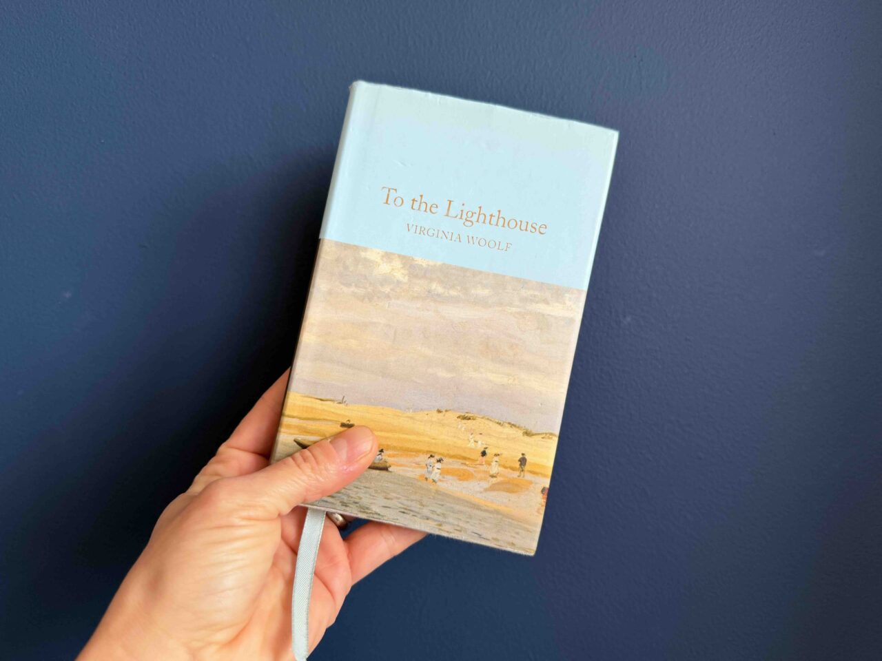 Cover of a hardback edition of To the Lighthouse held by my hand against a navy background