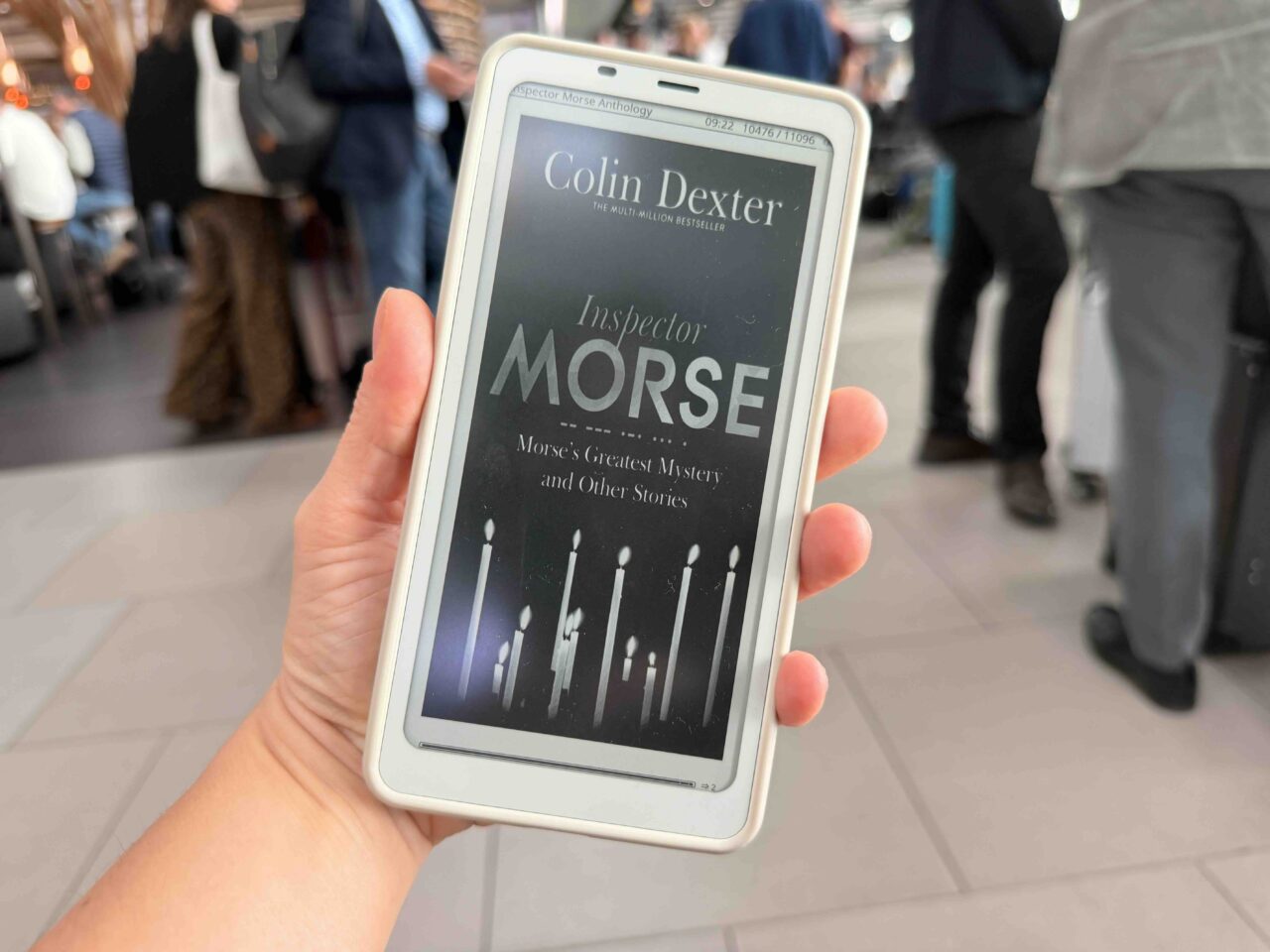 Morse's greatest mystery and other stories ebook cover held by my hand against a backdrop of people's legs in an airport lounge